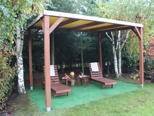 Pergola en bois avec toit en PVC beige, deux chaises longues et tables sur gazon dans un jardin