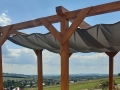 Vela ombreggiante grigia impermeabile ed estensibile su una pergola in legno con vista sul paesaggio