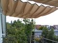 Vela ombreggiante da giardino beige estensibile su un balcone con vista sul panorama urbano e sugli alberi