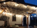 Vela ombreggiante beige impermeabile estensibile 2,5x3 m montata sotto la copertura del terrazzo con ghirlande luminose