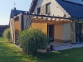 Rulou roman Premium impermeabil pentru terasă 2,5x4 m montat pe o pergolă din lemn lângă o casă modernă