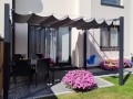 Rulou roman gri pentru terasă 2,5x4 m montat deasupra unui set de mobilier de grădină și leagăne lângă o casă modernă