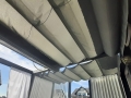 Rulou roman orizontal gri pentru terasă Premium montat pe o structură de pergolă cu vedere la cer și case