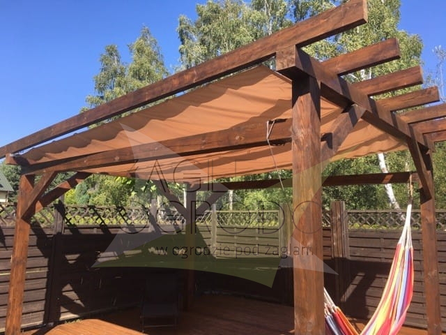 Pergola en bois marron avec voile d'ombrage rétractable beige sur une terrasse à côté d'un hamac coloré