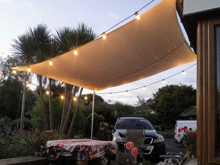 Toldo vela arena impermeable 3x4 m sobre la terraza, decorado con guirnaldas de luces ambientales por la noche