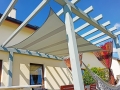 Toldo vela impermeable 3x3 m montado en una pérgola de madera junto a la casa con hamaca