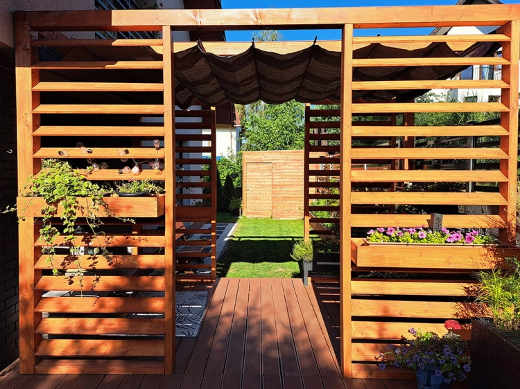 Bruin HDPE vouwgordijn als zonwering gemonteerd op een houten terraspergola bij de tuin