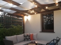 Wit zonnezeil voor overkapping op houten terrasconstructie met verlichting en tuinmeubelen