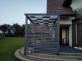 Wit zonnezeil voor overkapping gemonteerd op het dak van een moderne grafietkleurige terraspergola met een tuin op de achtergrond