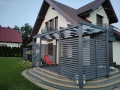 Popelavě šedý sluneční pás instalovaný na moderní dřevěné pergole u terasy domu