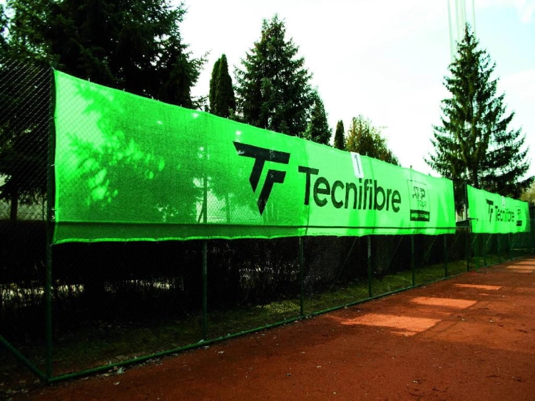 Bâche de tennis verte avec logo Tecnifibre, écran brise-vue sur mesure monté sur la clôture d'un court en terre battue