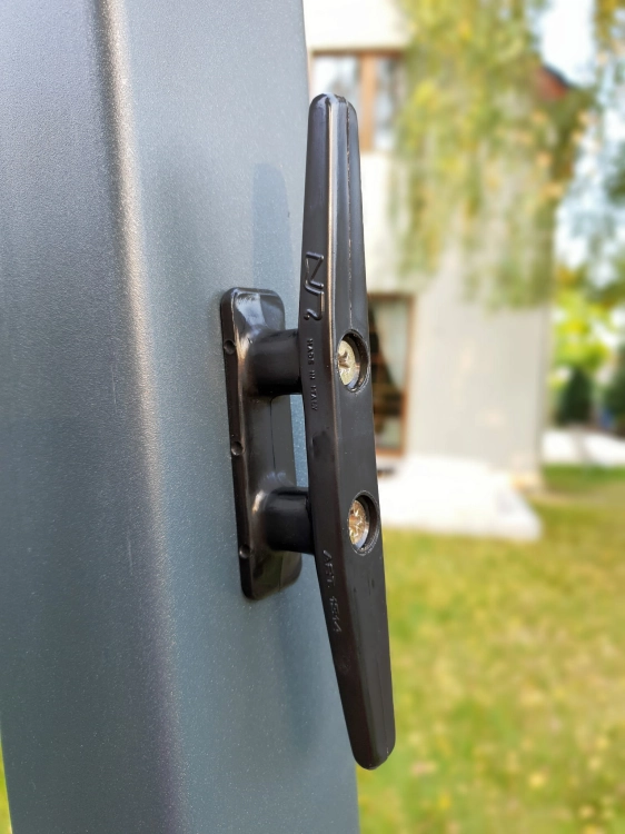 Czarna knaga do sznurka przykręcona do grafitowego profilu, element systemu bloczkowego do rolet rzymskich