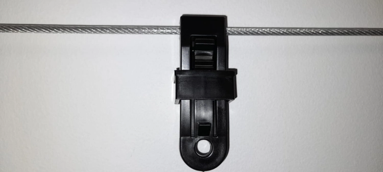 Schwarzer Seilstopper für Sonnensegel und Raffrollos, montiert an einem Stahlseil vor einer hellen Wand