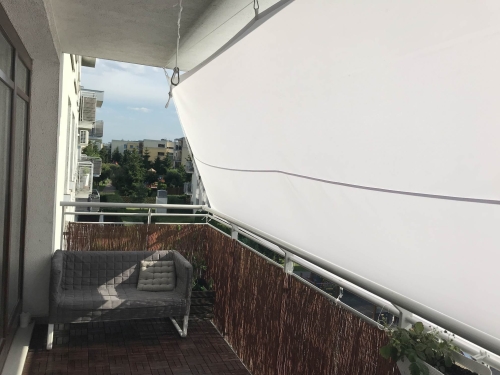 Voile d'ombrage imperméable sur mesure installée sur un balcon au-dessus d'un canapé gris et d'un sol en bois