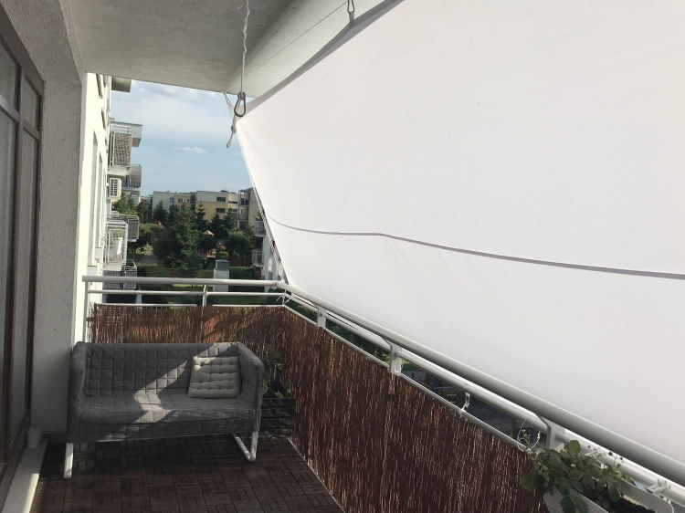 Voile d'ombrage imperméable sur mesure installée sur un balcon au-dessus d'un canapé gris et d'un sol en bois