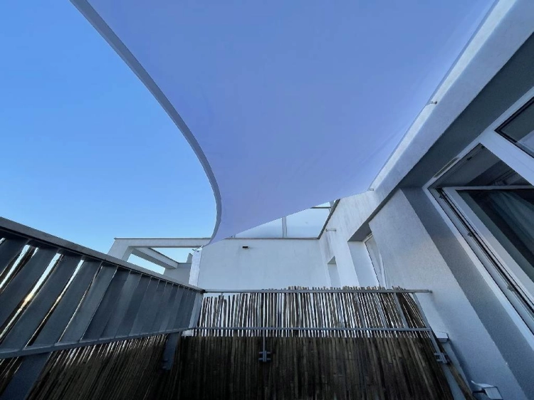 Voile d'ombrage imperméable sur mesure installée sur un balcon avec garde-corps en bois et façade claire