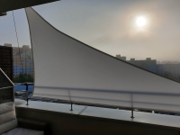 Voile d'ombrage triangulaire blanche montée sur une rampe de terrasse pour se protéger du soleil en ville