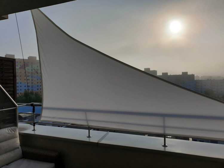 Voile d'ombrage triangulaire blanche montée sur une rampe de terrasse pour se protéger du soleil en ville