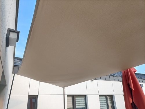 Voile d'ombrage beige imperméable sur mesure installée au-dessus de la terrasse d'un bâtiment moderne