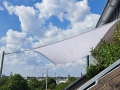 Pânză de umbrire dreptunghiulară albă pentru balcon, montată pe catarge lângă acoperiș cu vedere la panorama orașului