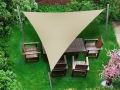 Toldo vela triangular beige sobre un conjunto de muebles de madera en un césped verde de jardín