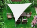 Vela de sombra triangular blanca sobre muebles de madera en el césped que proporciona sombra y protección solar