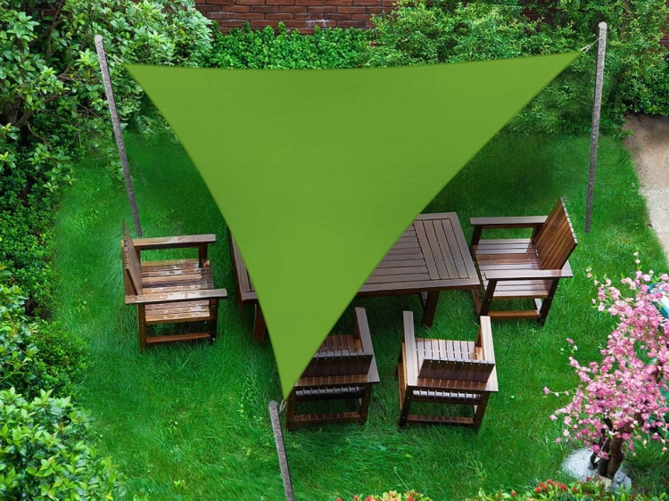 Toldo vela triangular verde sobre un conjunto de muebles de madera en el césped