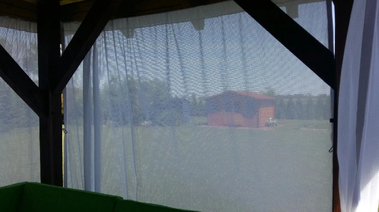 Rideau de terrasse blanc semi-transparent protégeant l'intérieur d'un gazebo de jardin en bois contre le soleil