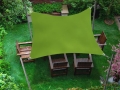 Voile d'ombrage carrée verte 3x3 m suspendue au-dessus de meubles en bois sur une pelouse de jardin
