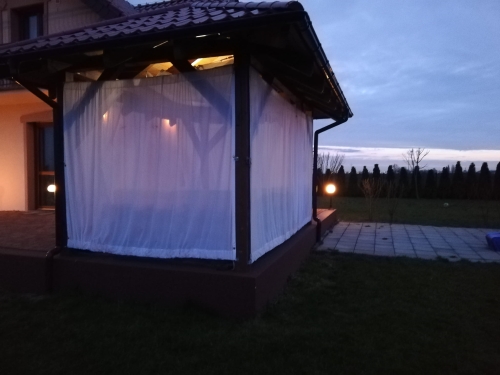 Cortina blanca de gasa para terraza que cubre un cenador de jardín iluminado al atardecer