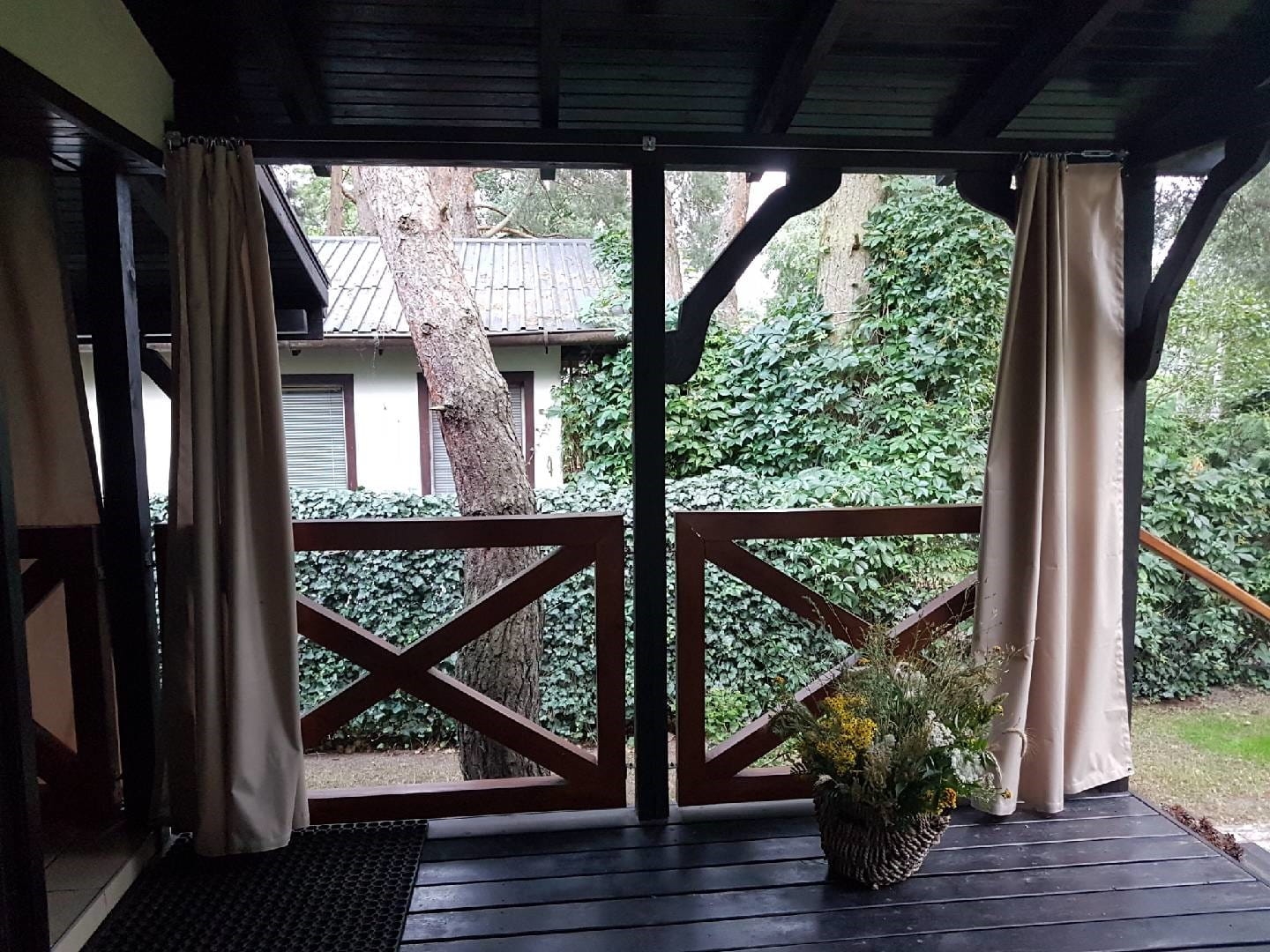 Waterdicht tuingordijn op maat gemonteerd op een houten terras bij een prieel in de kleur beige