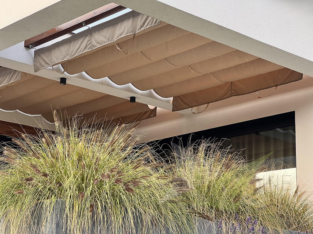Store romain de terrasse beige 3x4 m de type Premium protégeant du soleil et de la pluie au-dessus d'une terrasse avec plantes
