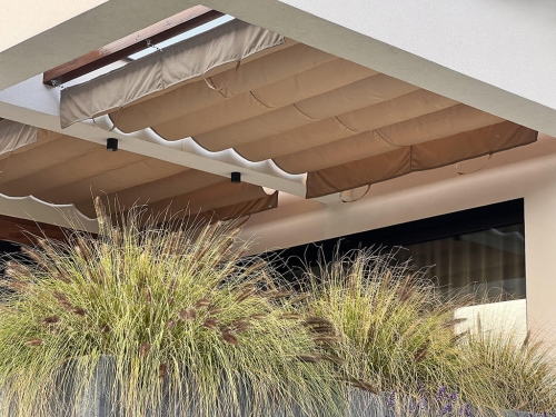 Store romarin de terrasse beige 4x4 m monté sous un toit de terrasse à côté d'herbes ornementales