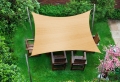 Toldo vela rectangular beige 4x7 m extendido sobre muebles de jardín de madera en el césped