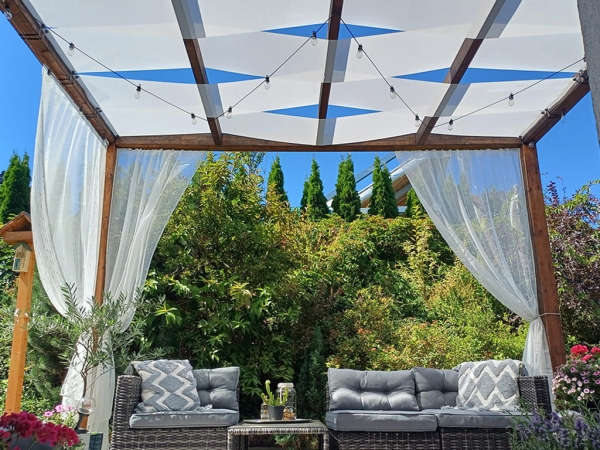 Bande pare-soleil blanche pour tonnelle installée sur une pergola en bois au-dessus d'un salon de jardin