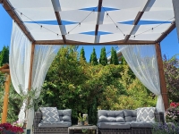 Voile d'ombrage blanc monté sur une pergola en bois au-dessus d'un salon de jardin en résine tressée