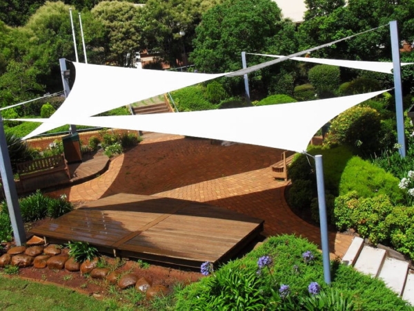 Voile d'ombrage triangulaire blanche sur mesure protégeant une terrasse et un plancher en bois dans le jardin