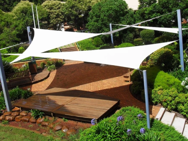 Weißes, dreieckiges Sonnensegel nach Maß beschattet eine Terrasse und ein Holzdeck im Garten