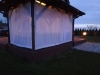 Cortina de terraza blanca hecha a medida instalada en un cenador de madera al anochecer