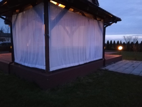 Cortina de terraza blanca hecha a medida instalada en un cenador de madera al anochecer
