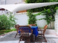 Velă de umbră triunghiulară albă deasupra unei terase cu mobilier din ratan și o masă albastră
