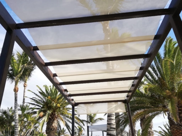 Store romain beige 2,1x5 m monté sur une pergola de terrasse marron entourée de palmiers