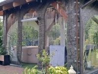 Bâche de terrasse transparente avec impression imitation pierre, protégeant un gazébo avec jacuzzi et mobilier de jardin