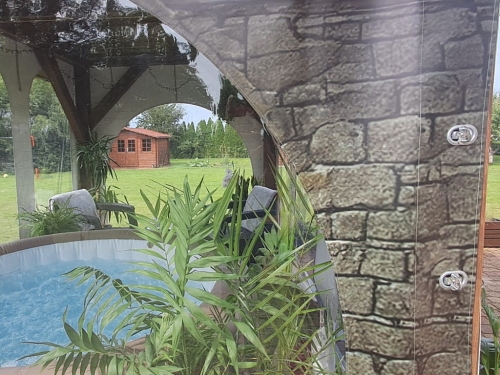 Bâche de terrasse transparente avec motif de mur abritant un jacuzzi dans un jardin avec vue sur un gazebo et des plantes