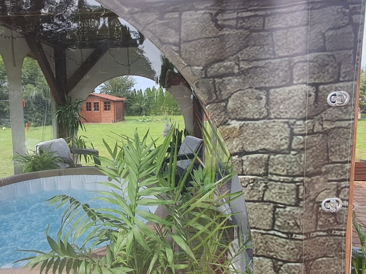 Bâche de terrasse transparente avec motif de mur abritant un jacuzzi dans un jardin avec vue sur un gazebo et des plantes