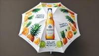 Witte reclameparasol met opdruk van tropisch fruit en een fles Deskeka-drank op een grijze achtergrond