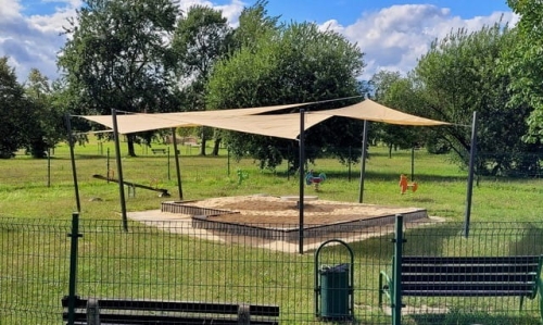 Bac à sable sur un terrain de jeux abrité par une voile d'ombrage beige sur mesure montée sur des poteaux