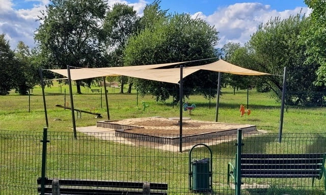 Bac à sable sur un terrain de jeux abrité par une voile d'ombrage beige sur mesure montée sur des poteaux