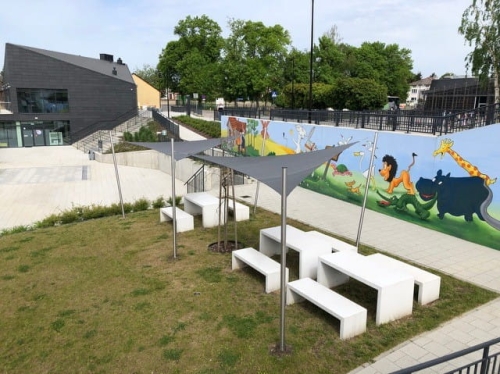 Voiles d'ombrage gris sur mesure au-dessus de tables et bancs blancs sur une aire de jeux moderne.