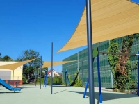 Voiles d'ombrage claires sur mesure installées au-dessus d'une aire de jeux moderne avec balançoires et toboggan